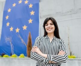 Girl standing in front of the European Union flag and talking about the best countries to study in Europe