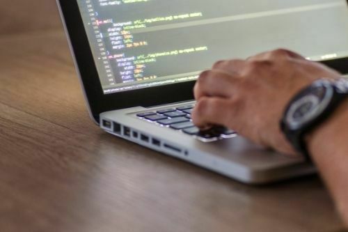 a laptop kept on table and a student from webs designing course writing a css on laptop, wearing a black colored watch in hands.